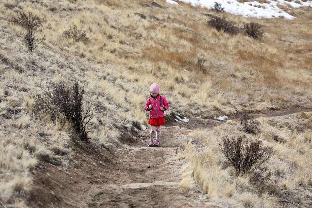 Ein junges Mädchen in pinker Wanderjacke und mit einem kleinen Rucksack auf einem Bergpfad.